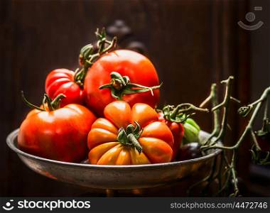 Fresh organic farm tomatoes in steel bowl over dark wooden background, close up