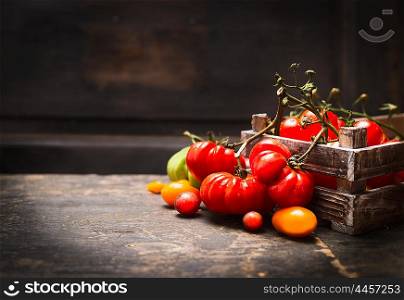 Fresh organic garden tomatoes in vintage box on rustic table over dark wooden background. Healthy and vegetarian food concept.