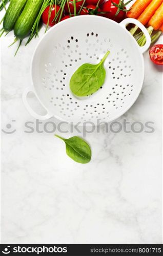 fresh organic garden vegetables and colander bowl on white rustic stone background, healthy cooking concept