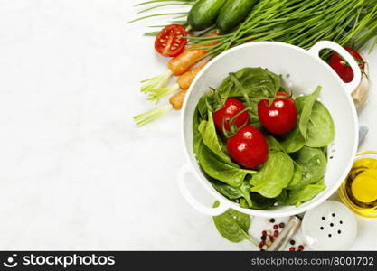 fresh organic garden vegetables in colander bowl on white rustic stone background, healthy cooking concept