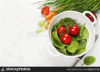 fresh organic garden vegetables in colander bowl on white rustic stone background, healthy cooking concept