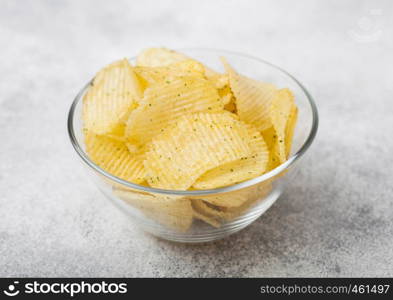 Fresh organic homemade potato crisps chips in glass bowl on light table background.