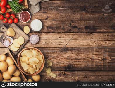 Fresh organic homemade potato crisps chips in wooden bowl with sour cream and red onions and spices on wooden background. Space for text