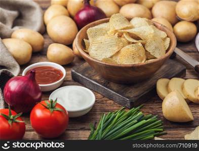 Fresh organic homemade potato crisps chips in wooden bowl with sour cream and red onions and spices on wooden background.