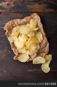 Fresh organic homemade potato crisps chips on paper on wooden background.