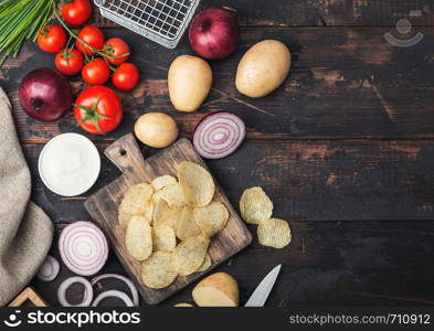 Fresh organic homemade potato crisps chips with sour cream and red onions on chopping board on dark wooden background. Space for text