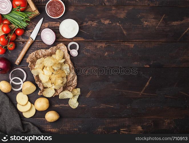 Fresh organic homemade potato crisps chips with sour cream and red onions on paper on wooden background. Space for text