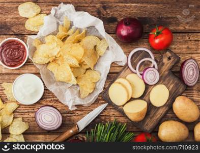 Fresh organic homemade potato crisps chips with sour cream and red onions and spices on wooden table background.