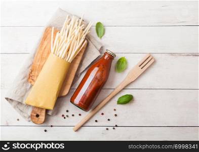 Fresh organic homemade spaghetti pasta with bottle of tomato sauce and wooden spatula and basil leaf on wooden board background.