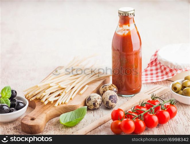 Fresh organic homemade spaghetti pasta with quail eggs and fresh tomatoes with bottle of tomato sauce and wooden spatula and basil leaf on wooden board background. Classic italian food