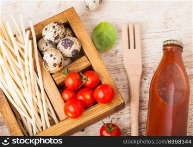 Fresh organic hommemade spaghetti pasta with quail eggs and fresh tomatoes with bottle of tomato sauce and wooden spatula and basil leaf on wooden board background. Classic italian food