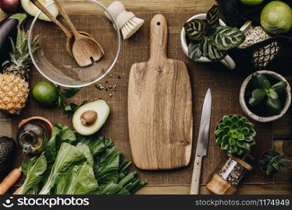 Fresh organic ingredients for salad making and wooden spoons with glass salad bowl on rustic background, top view. Flat lay with place for text. Vegan and healthy food layout