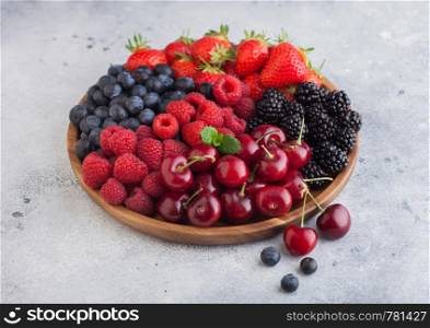 Fresh organic summer berries mix in round wooden tray on light kitchen table background. Raspberries, strawberries, blueberries, blackberries and cherries. Top view