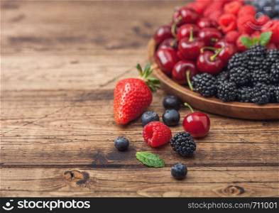 Fresh organic summer berries mix in round wooden tray on light wooden table background. Raspberries, strawberries, blueberries, blackberries and cherries. Top view