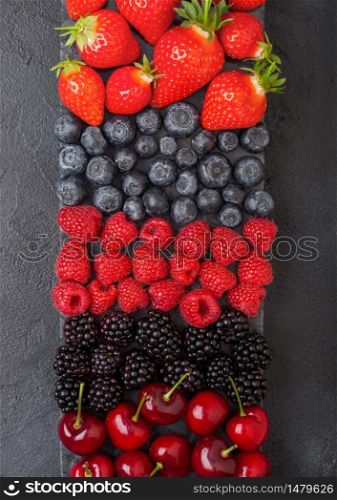 Fresh organic summer berries mix on black marble board on dark kitchen table background. Raspberries, strawberries, blueberries, blackberries and cherries. Top view