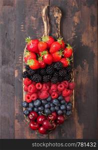Fresh organic summer berries mix on vintage wooden chopping board on dark wooden table background. Raspberries, strawberries, blueberries, blackberries and cherries.Top view