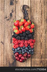 Fresh organic summer berries mix on vintage wooden chopping board on light wooden table background. Raspberries, strawberries, blueberries, blackberries and cherries.Top view
