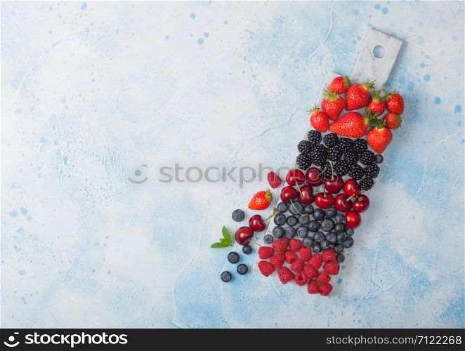Fresh organic summer berries mix on white marble board on blue kitchen table background. Raspberries, strawberries, blueberries, blackberries and cherries. Top view