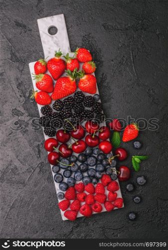 Fresh organic summer berries mix on white marble board on dark kitchen table background. Raspberries, strawberries, blueberries, blackberries and cherries. Top view