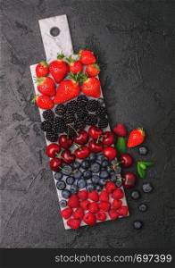 Fresh organic summer berries mix on white marble board on dark kitchen table background. Raspberries, strawberries, blueberries, blackberries and cherries. Top view