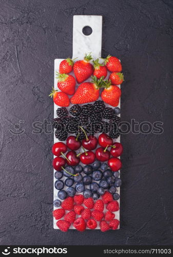 Fresh organic summer berries mix on white marble board on dark kitchen table background. Raspberries, strawberries, blueberries, blackberries and cherries. Top view