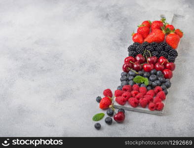 Fresh organic summer berries mix on white marble board on light kitchen table background. Raspberries, strawberries, blueberries, blackberries and cherries. Top view