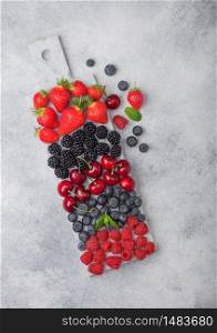 Fresh organic summer berries mix on white marble board on light kitchen table background. Raspberries, strawberries, blueberries, blackberries and cherries. Top view