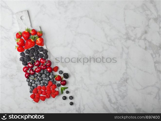 Fresh organic summer berries mix on white marble board on marble background. Raspberries, strawberries, blueberries, blackberries and cherries. Top view