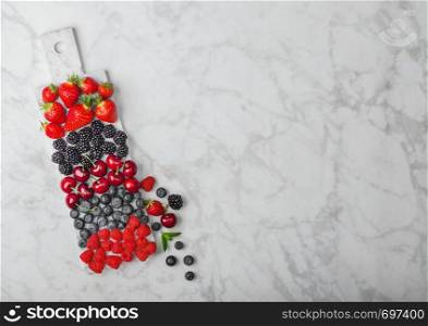 Fresh organic summer berries mix on white marble board on marble background. Raspberries, strawberries, blueberries, blackberries and cherries. Top view