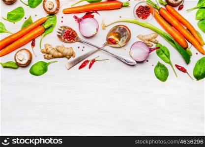 Fresh organic vegetables and spoons on white wooden background, top view, border. Healthy food or vegetarian cooking concept.