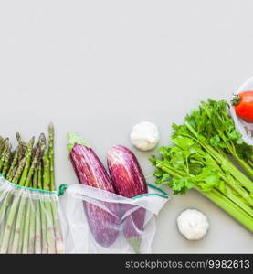 Fresh organic vegetables in eco reusable produce shopping bags flat lay, top view with copy space on gray background. Sustainable lifestyle. Zero waste, plastic free concept.