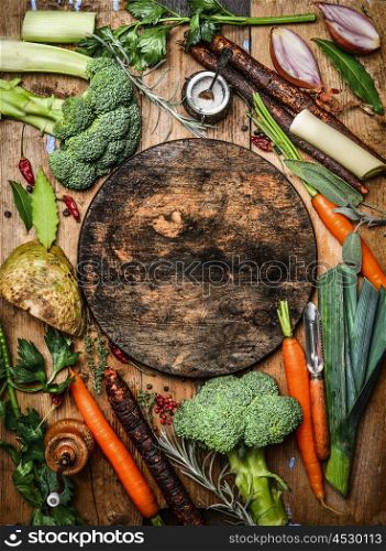 Fresh organic vegetables ingredients for soup or broth around round rustic blank cutting board, top view. Healthy food or vegetarian cooking concept.