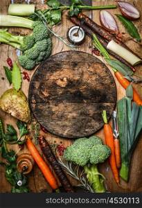 Fresh organic vegetables ingredients for soup or broth around round rustic blank cutting board, top view. Healthy food or vegetarian cooking concept.