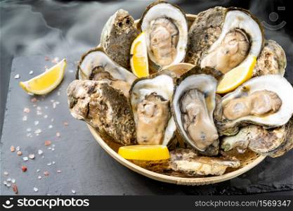 Fresh oyster serve with lemon in basket on black stone plate. Fresh seafood food and european cuisine gourmet concept.