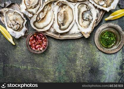 Fresh oysters with lemon and various sauces on rustic background, top view, place for text , border