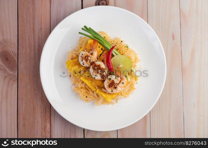 Fresh Pad Thai Shrimp with lime, lettuce, omelet and spring onions in a white plate on wooden.