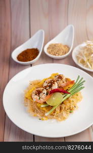 Fresh Pad Thai Shrimp with lime, lettuce, omelet and spring onions in a white plate on wooden.