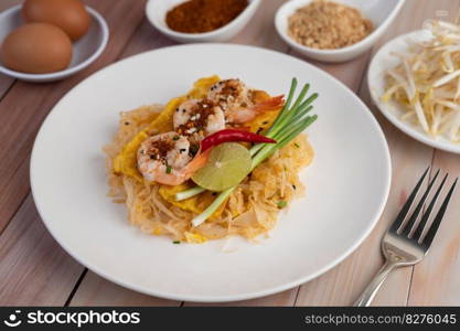 Fresh Pad Thai Shrimp with lime, lettuce, omelet and spring onions in a white plate on wooden.