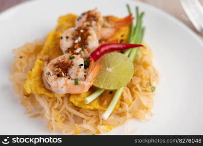 Fresh Pad Thai Shrimp with lime, lettuce, omelet and spring onions in a white plate on wooden.