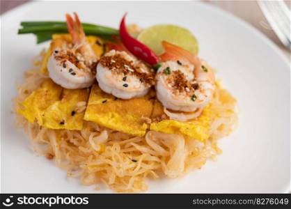 Fresh Pad Thai Shrimp with lime, lettuce, omelet and spring onions in a white plate on wooden.