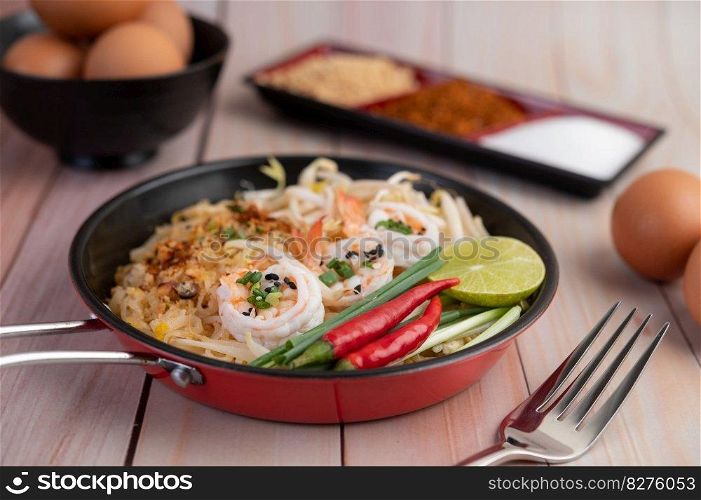 Fresh Pad Thai Shrimp with lime, lettuce, omelet and spring onions in a pan on wooden.