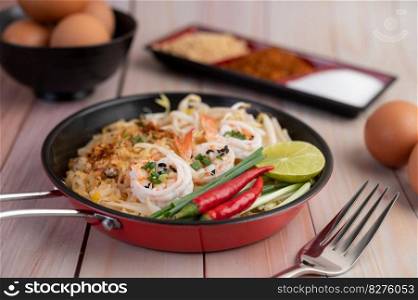 Fresh Pad Thai Shrimp with lime, lettuce, omelet and spring onions in a pan on wooden.