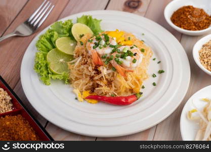 Fresh Pad Thai Shrimp with lime, lettuce, omelet and spring onions in a white plate on wooden.