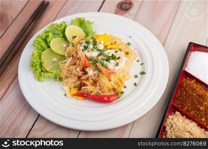 Fresh Pad Thai Shrimp with lime, lettuce, omelet and spring onions in a white plate on wooden.