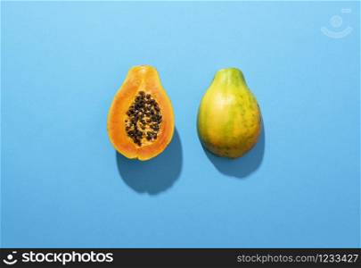 Fresh papaya fruit cut in half, isolated on a blue background, in sunlight. Juicy tropical fruit. Sweet summer fruit. Exotic fruit. Halves of papaya.