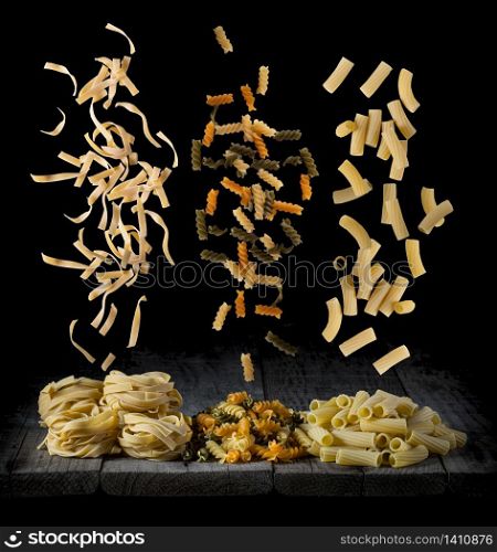 fresh pasta falling in different shapes and colours on a wood in front of a black background