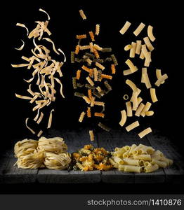 fresh pasta falling in different shapes and colours on a wood in front of a black background