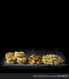 fresh pasta of different shapes and colours on a wood in front of a black background