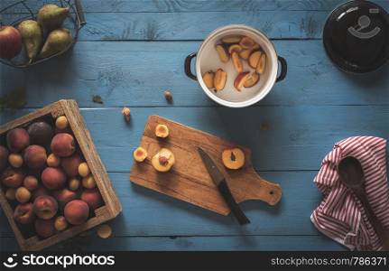 Fresh peaches and apricots in a wooden box, sliced fruits on cutting boards for making peach marmalade on a blue table. Above view home cooking jam.