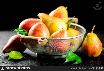 Fresh pears with leaves in a colander. On a black background. High quality photo. Fresh pears with leaves in a colander.